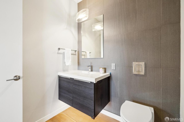 bathroom featuring toilet, wood finished floors, vanity, and tile walls