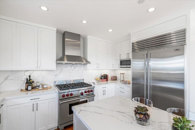 kitchen featuring wall chimney exhaust hood, high quality appliances, white cabinetry, and tasteful backsplash