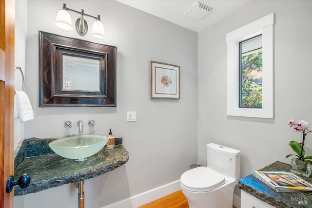 bathroom with visible vents, toilet, a sink, wood finished floors, and baseboards