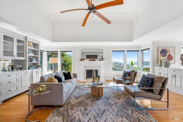 living area with light wood-style floors, a fireplace, crown molding, and a towering ceiling