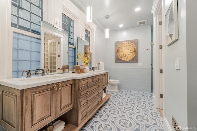 bathroom with visible vents, double vanity, toilet, tile walls, and a wainscoted wall