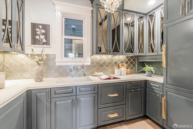 kitchen featuring light countertops, a sink, gray cabinetry, and glass insert cabinets