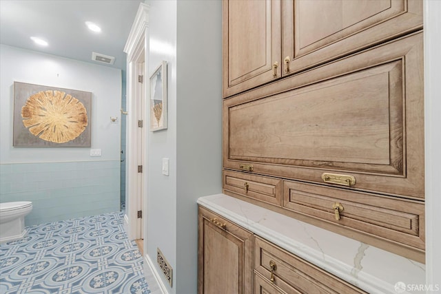 full bath with tile walls, toilet, and visible vents