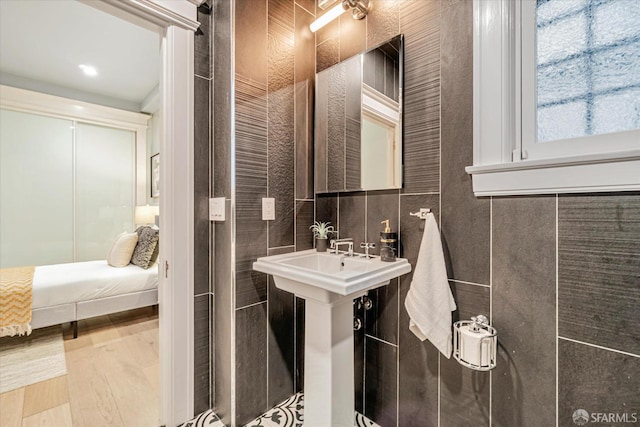 ensuite bathroom with a sink, ensuite bath, wood finished floors, and tile walls