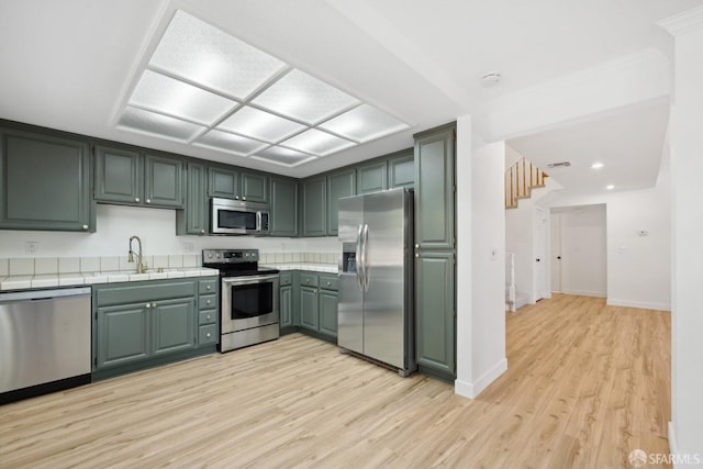 kitchen with appliances with stainless steel finishes, light wood-type flooring, a sink, baseboards, and tile counters