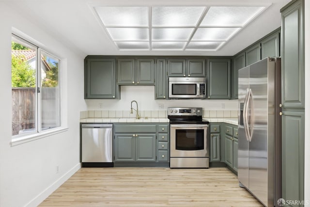 kitchen with tile counters, a sink, appliances with stainless steel finishes, and light wood-style flooring