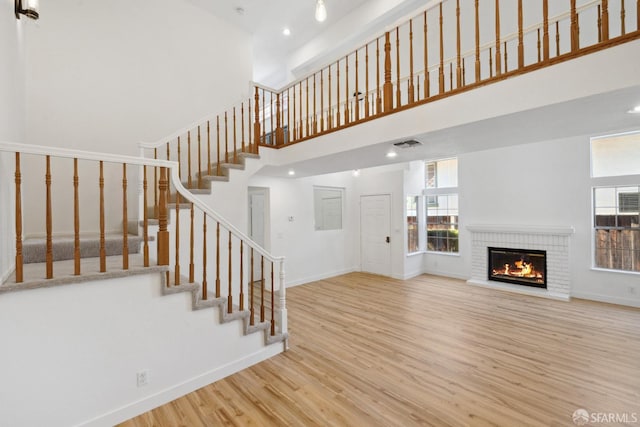 unfurnished living room featuring visible vents, wood finished floors, a fireplace, a high ceiling, and stairway