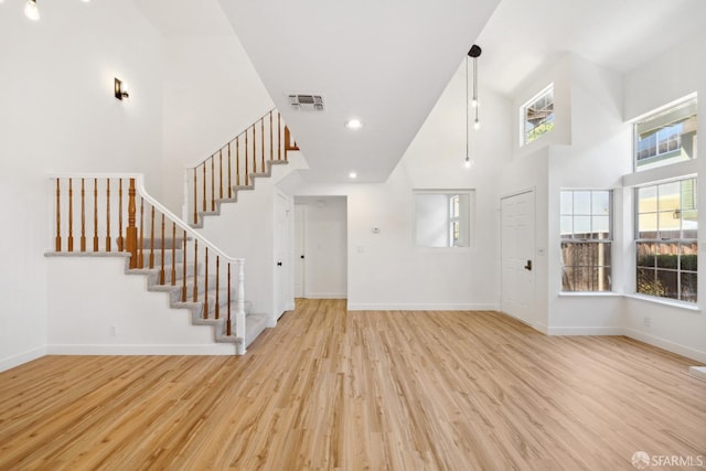 unfurnished living room with light wood-style floors, stairs, baseboards, a towering ceiling, and visible vents