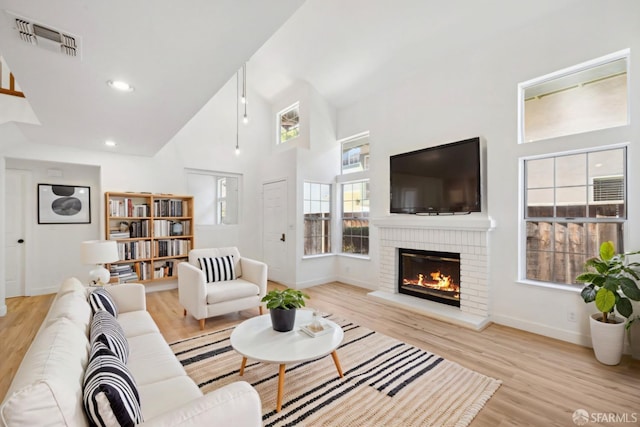 living room with visible vents, baseboards, light wood finished floors, and high vaulted ceiling