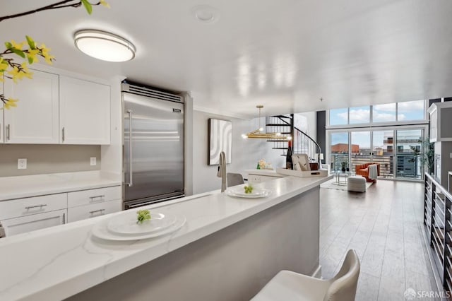 kitchen featuring hardwood / wood-style flooring, white cabinetry, light stone counters, decorative light fixtures, and built in fridge