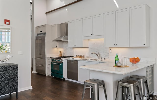 kitchen with wall chimney exhaust hood, a breakfast bar, premium appliances, sink, and white cabinets