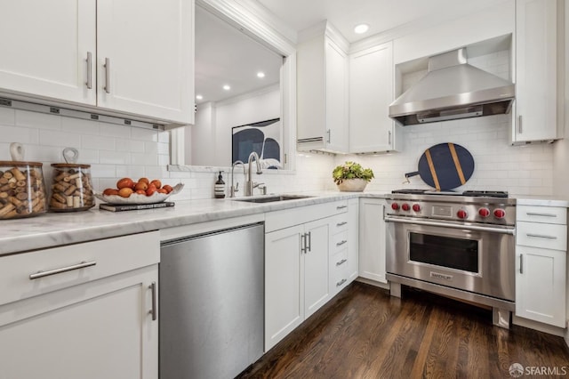 kitchen featuring white cabinets, wall chimney exhaust hood, appliances with stainless steel finishes, dark wood-type flooring, and a sink