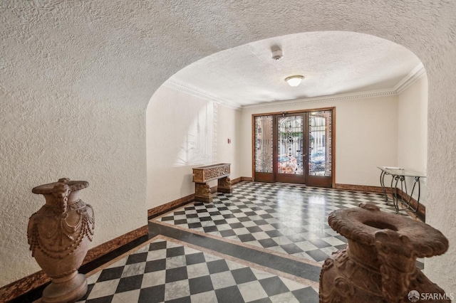 entryway featuring arched walkways, a textured wall, a textured ceiling, baseboards, and ornamental molding