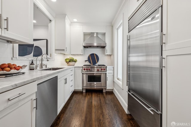 kitchen featuring premium appliances, light stone counters, white cabinetry, a sink, and wall chimney range hood