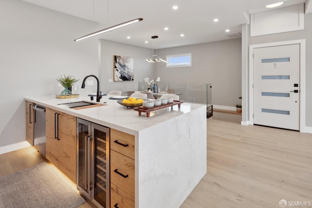 kitchen featuring sink, wine cooler, light stone countertops, decorative light fixtures, and light brown cabinets