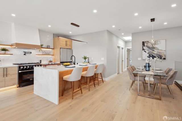 kitchen featuring stainless steel fridge, premium range hood, hanging light fixtures, high end stove, and light brown cabinets