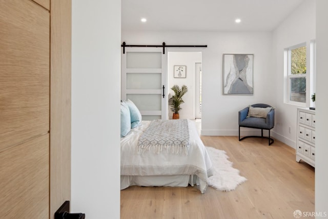 bedroom with a barn door and light wood-type flooring