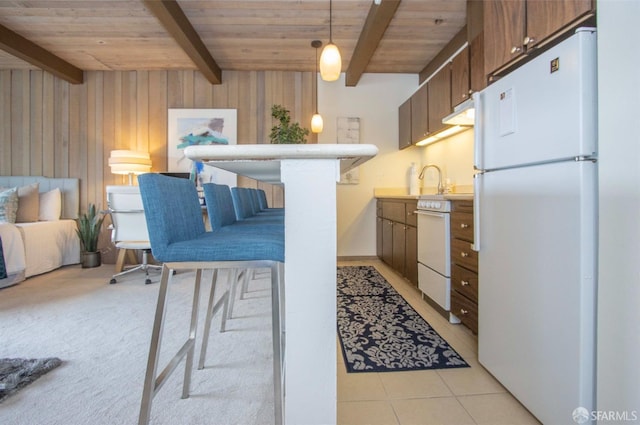 kitchen featuring beam ceiling, a kitchen breakfast bar, white refrigerator, and wood walls