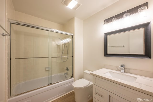 bathroom featuring visible vents, toilet, combined bath / shower with glass door, vanity, and wood finished floors