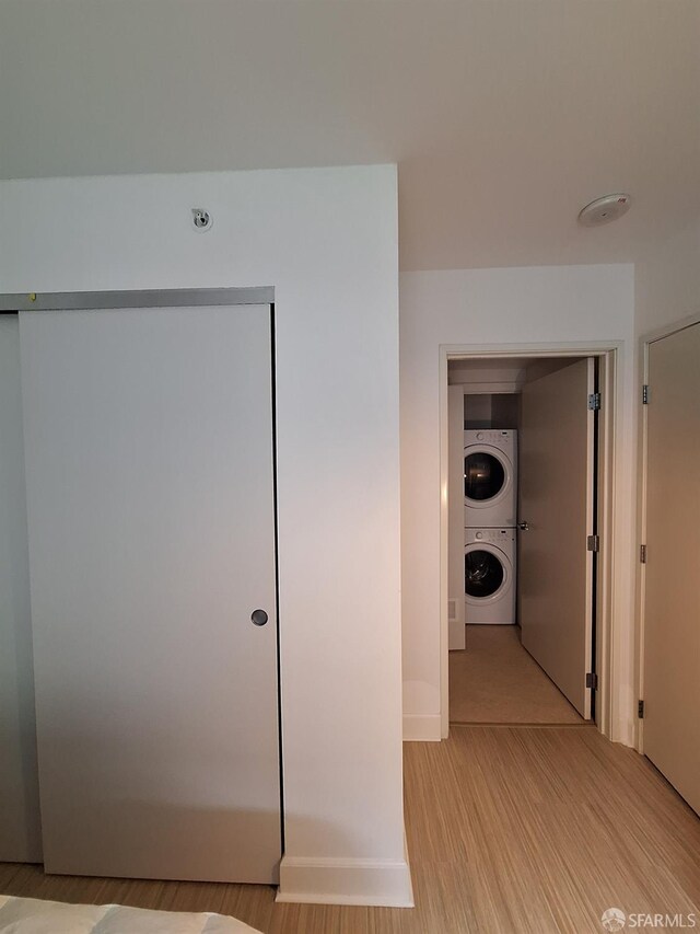 hallway with stacked washer / drying machine and light wood-type flooring