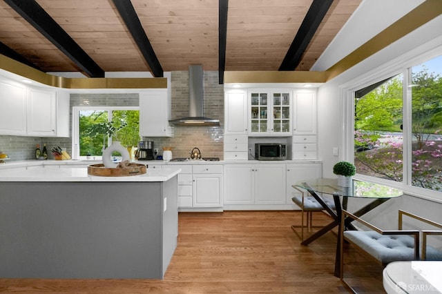 kitchen with wall chimney range hood, decorative backsplash, wooden ceiling, light countertops, and stainless steel microwave