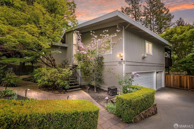 view of side of home featuring a garage, aphalt driveway, stairway, and fence