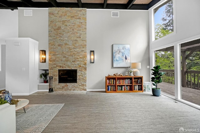 living room featuring visible vents, a stone fireplace, a high ceiling, and beam ceiling