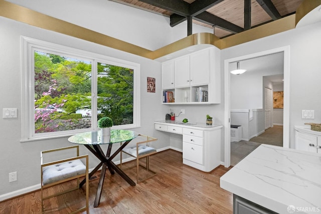 kitchen featuring built in desk, light stone counters, white cabinetry, light wood-style floors, and beamed ceiling
