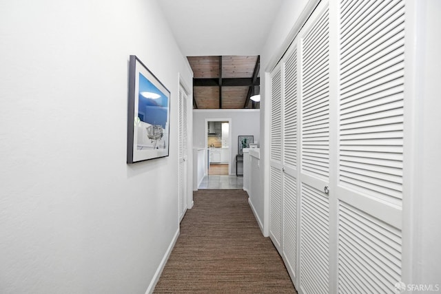 corridor with dark colored carpet, baseboards, and beam ceiling