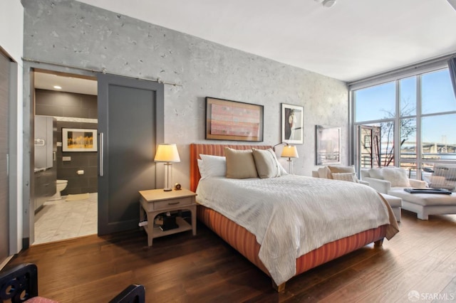 bedroom with dark hardwood / wood-style flooring, expansive windows, a barn door, and connected bathroom