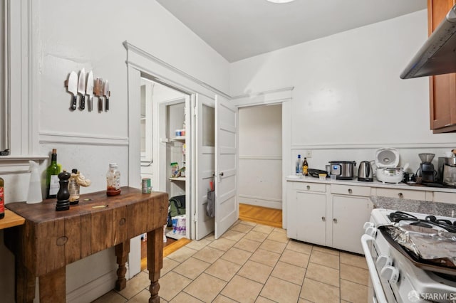 kitchen with light tile patterned floors, white cabinets, light countertops, range hood, and gas range gas stove