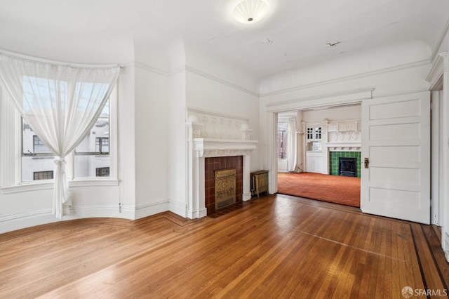 unfurnished living room with a tile fireplace, baseboards, and wood finished floors