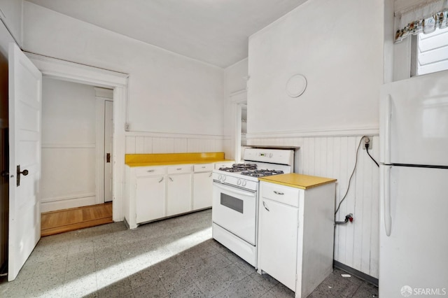 kitchen featuring white appliances, light countertops, light floors, and a wainscoted wall