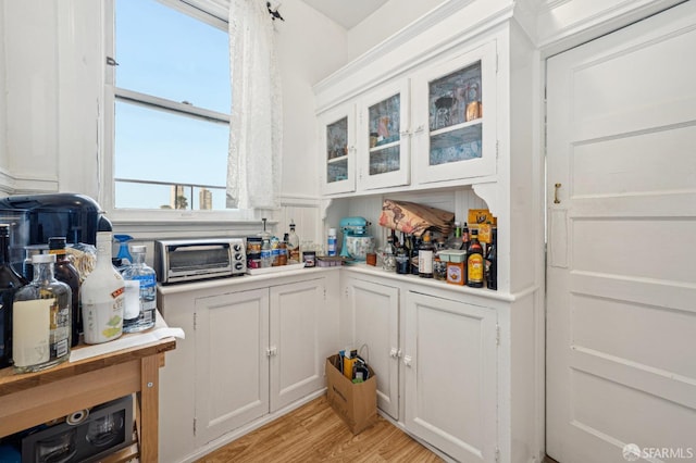 kitchen with a toaster, white cabinets, glass insert cabinets, light countertops, and light wood-style floors