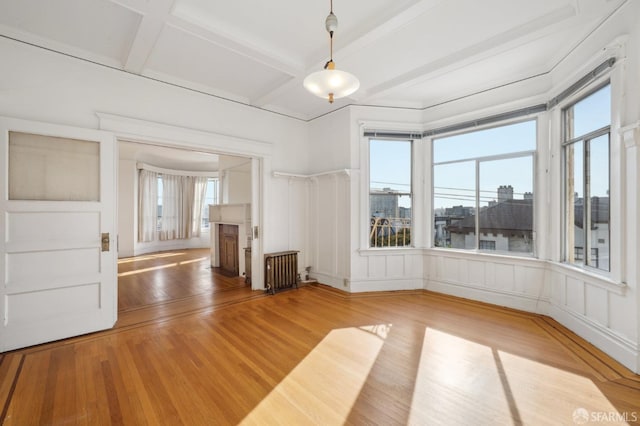 interior space with beam ceiling, light wood finished floors, radiator, a decorative wall, and coffered ceiling