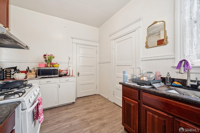 kitchen with light wood-style flooring, under cabinet range hood, a wainscoted wall, stainless steel microwave, and white gas range