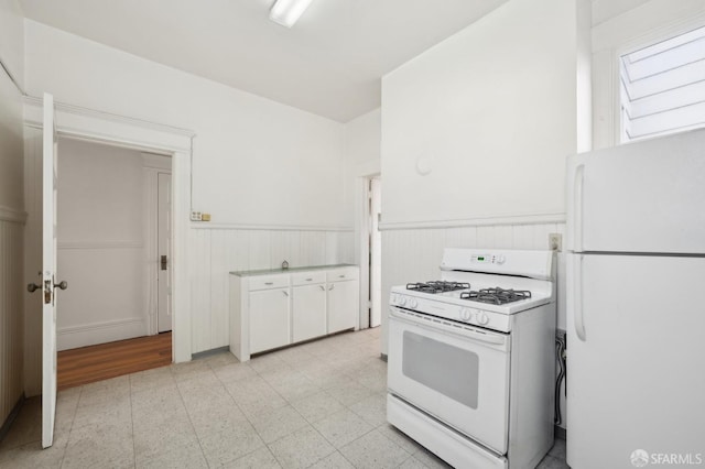 kitchen featuring a wainscoted wall, light floors, white appliances, and white cabinets