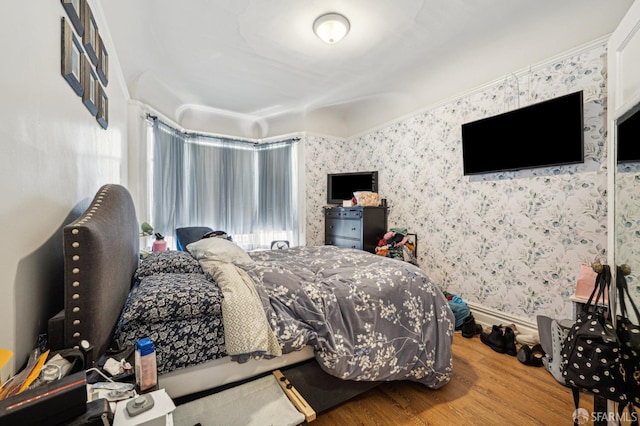 bedroom with baseboards, wood finished floors, and wallpapered walls