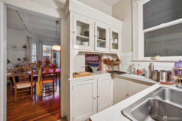 kitchen with coffered ceiling, a sink, white cabinetry, light countertops, and glass insert cabinets