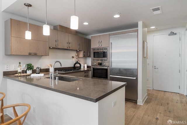 72 Townsend St Unit 302, San Francisco, CA 94107 - kitchen with built in appliances, a peninsula, dark countertops, light wood-type flooring, and a sink