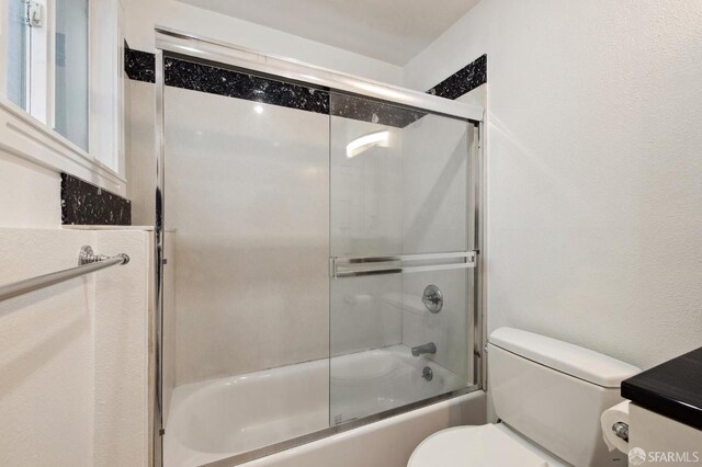 bathroom with bath / shower combo with glass door and toilet