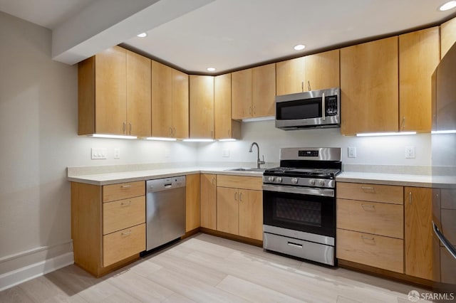 kitchen with appliances with stainless steel finishes, sink, light brown cabinets, and light hardwood / wood-style flooring