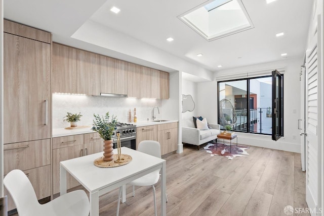 kitchen featuring sink, light hardwood / wood-style flooring, backsplash, a skylight, and light brown cabinetry