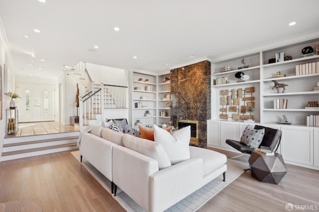 living room featuring crown molding, built in shelves, a high end fireplace, and light hardwood / wood-style flooring