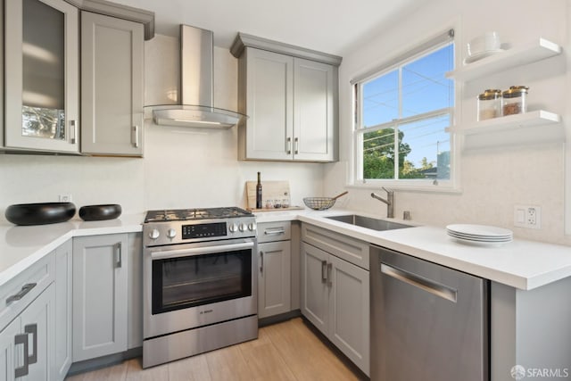 kitchen with wall chimney exhaust hood, sink, light wood-type flooring, appliances with stainless steel finishes, and gray cabinets