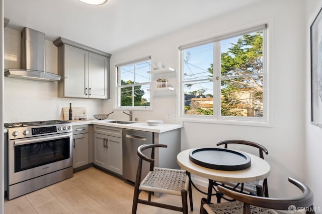 kitchen featuring sink, light wood-type flooring, gray cabinets, stainless steel appliances, and wall chimney range hood