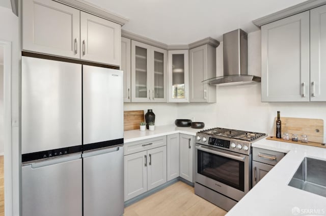 kitchen with sink, appliances with stainless steel finishes, gray cabinets, light hardwood / wood-style floors, and wall chimney range hood