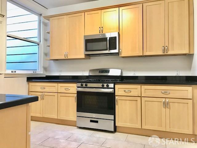 kitchen featuring appliances with stainless steel finishes, light brown cabinetry, dark countertops, and light tile patterned floors