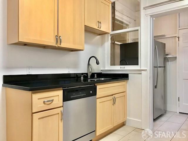 kitchen with dishwasher, light tile patterned floors, light brown cabinetry, and dark countertops