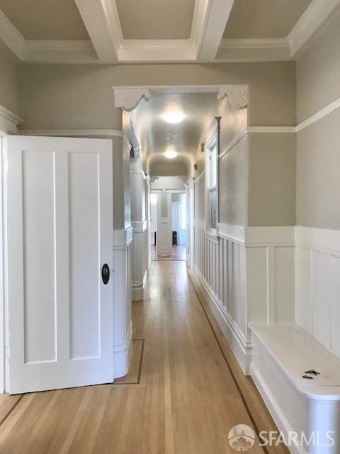 corridor with light wood-type flooring, ornamental molding, a decorative wall, and wainscoting